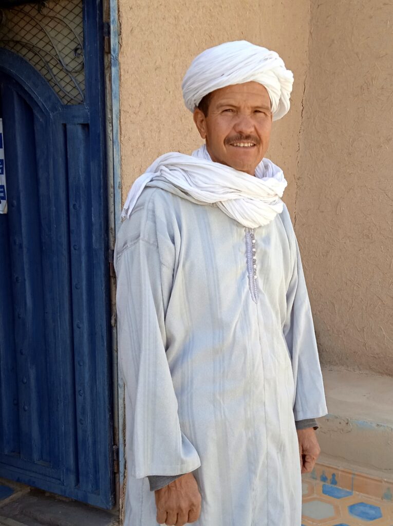 Ali accueille les voyageurs devant la porte d'entrée de l'auberge La vallée des Dunes, à Hassilabied, aux portes du Sahara